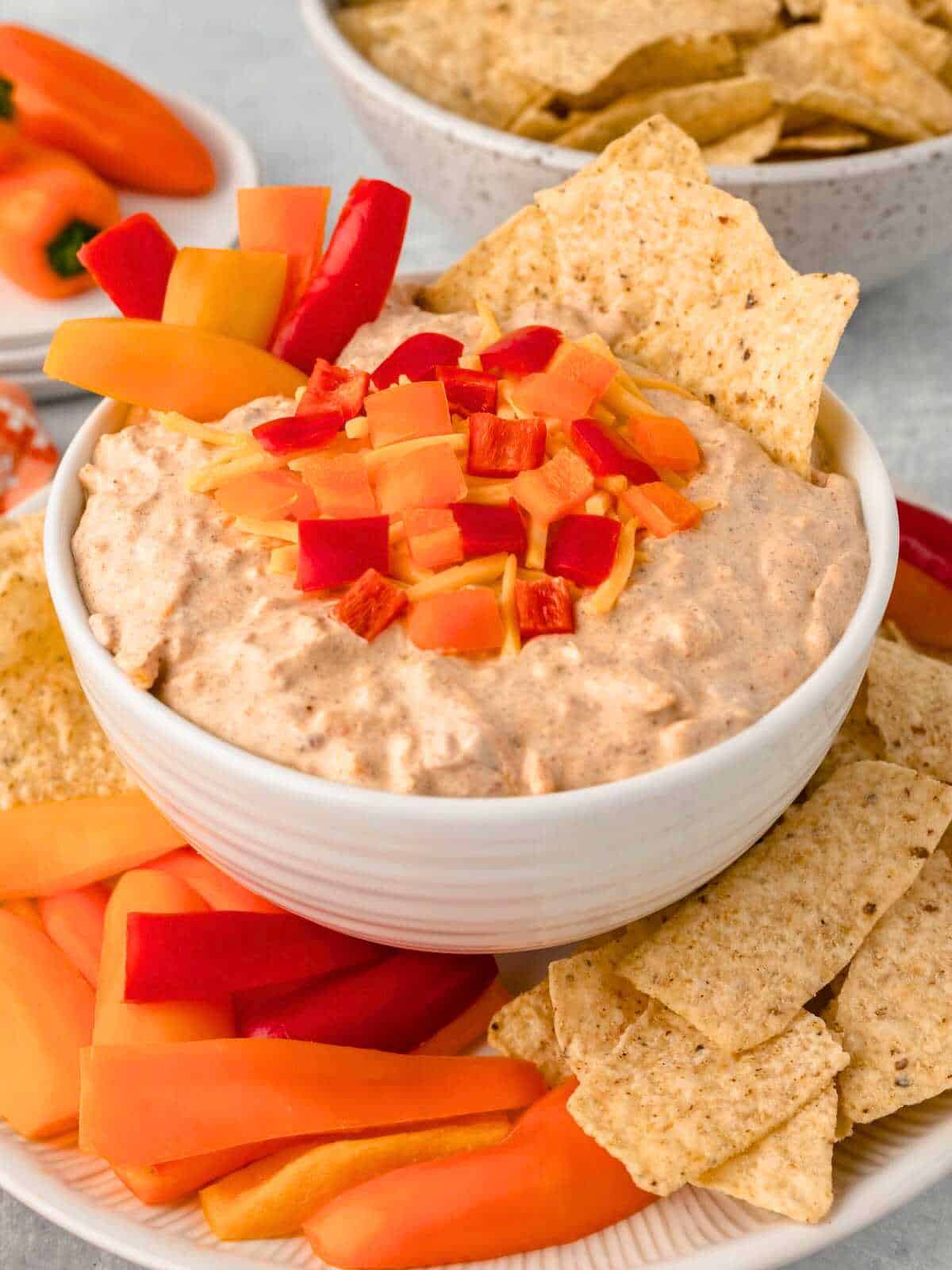 Boat dip with chopped peppers and tortilla chips on a white plate.