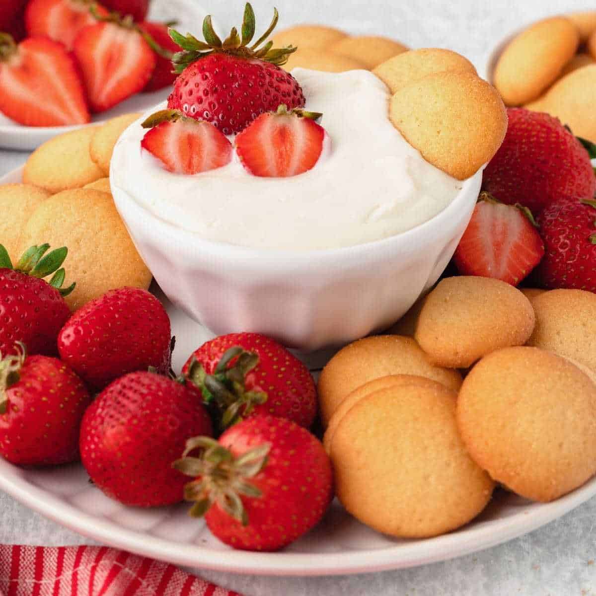 Cheesecake fruit dip in a white bowl surrounded by vanilla wafers and strawberries.