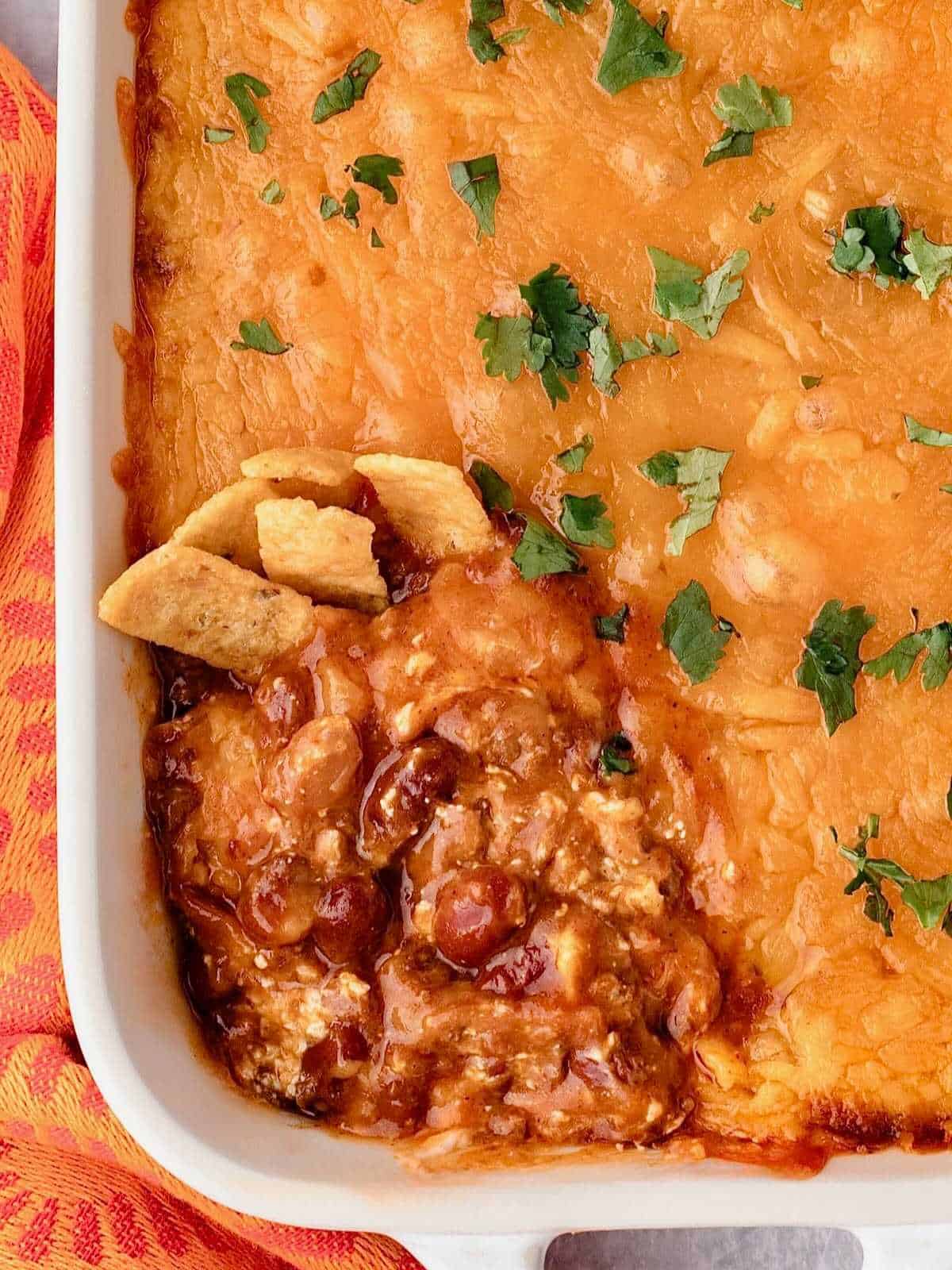 Chili cream cheese dip in a white baking dish with top layer of cheese removed to show chili underneath.