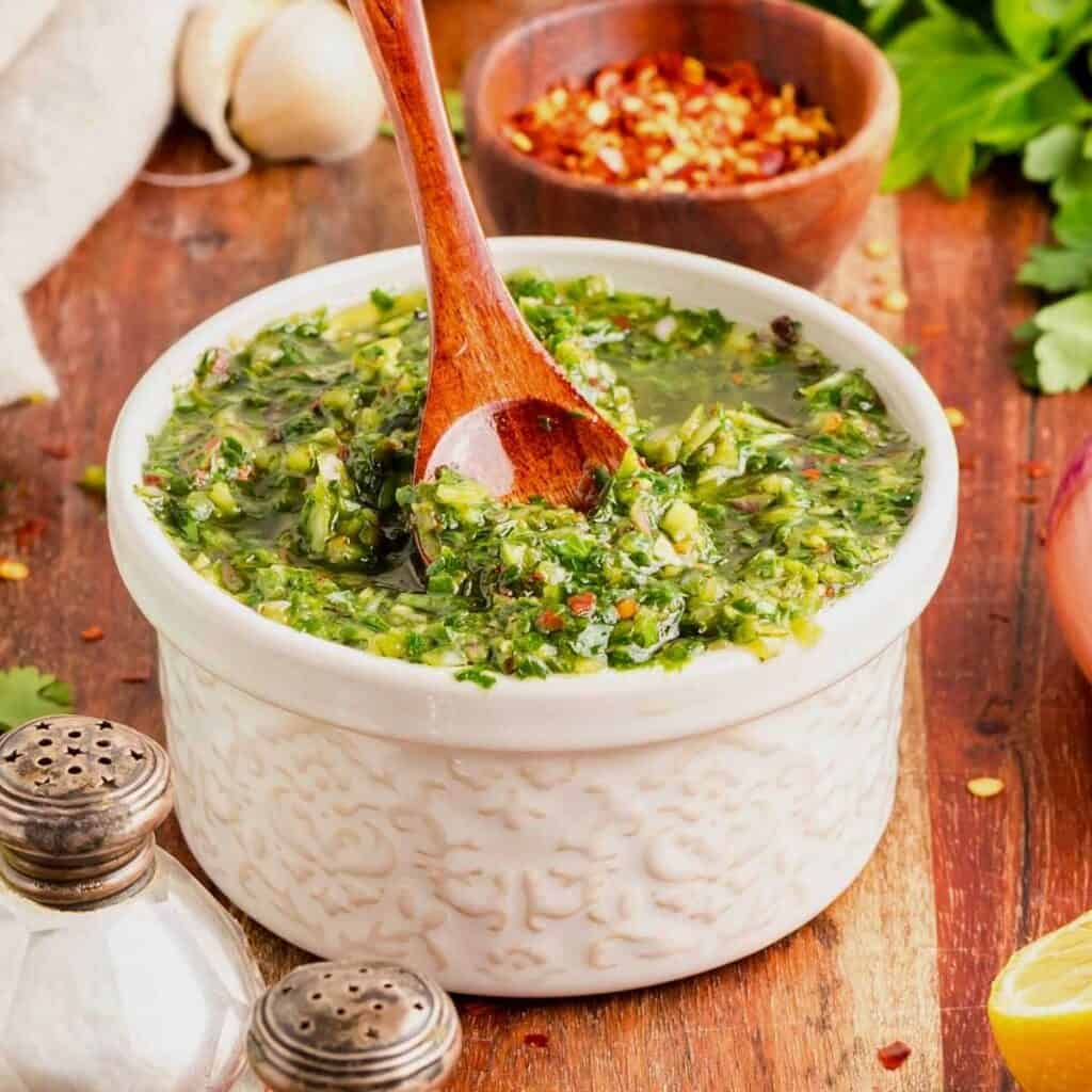 Bowl of green cilantro chimichurri sauce with a wooden spoon.