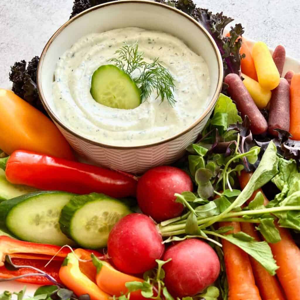 Cottage cheese ranch dip in a white bowl surrounded by colorful veggies.