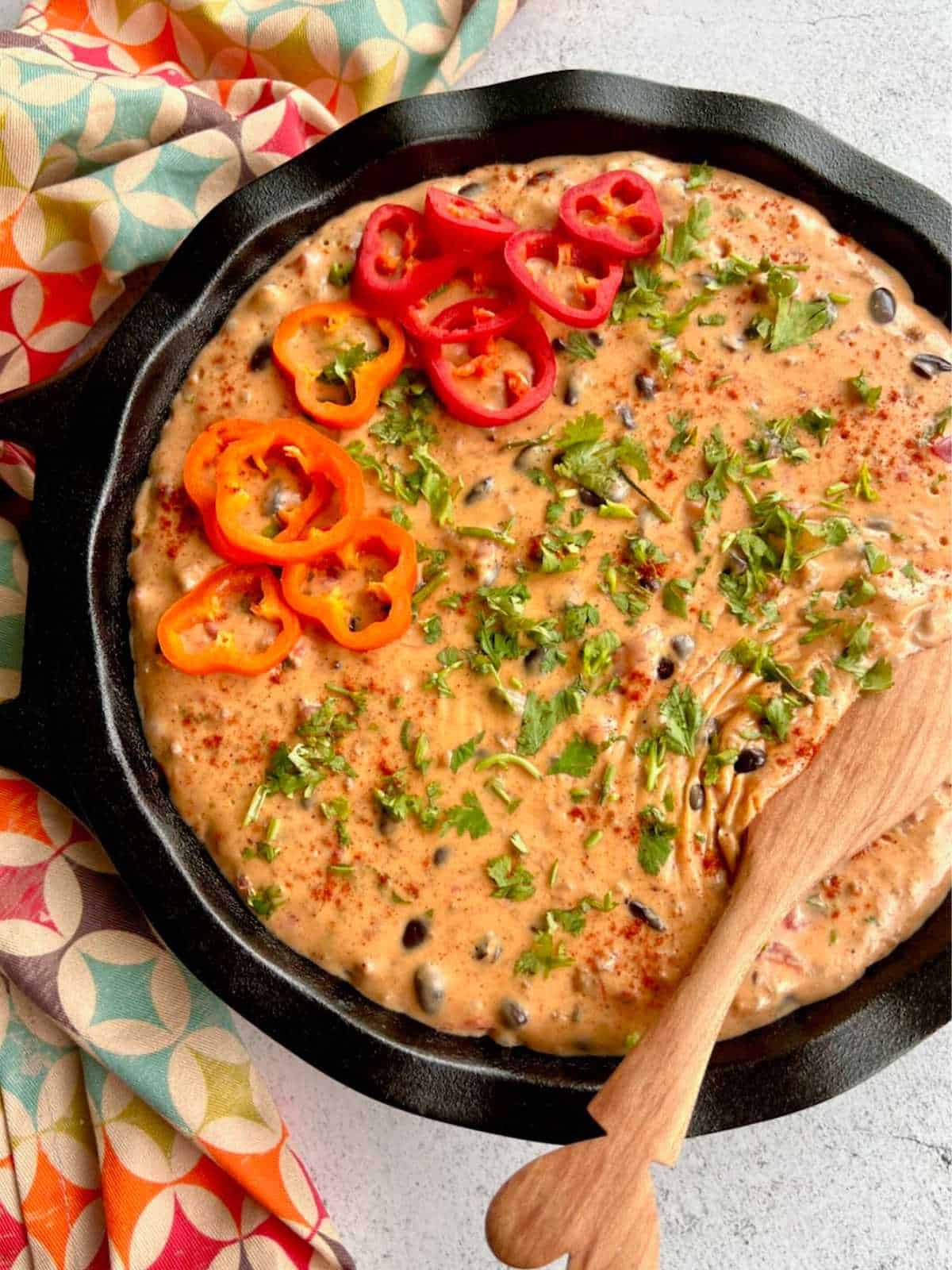 Wooden spoon lifting up Velveeta dip with Ro-tel in a cast iron skillet.
