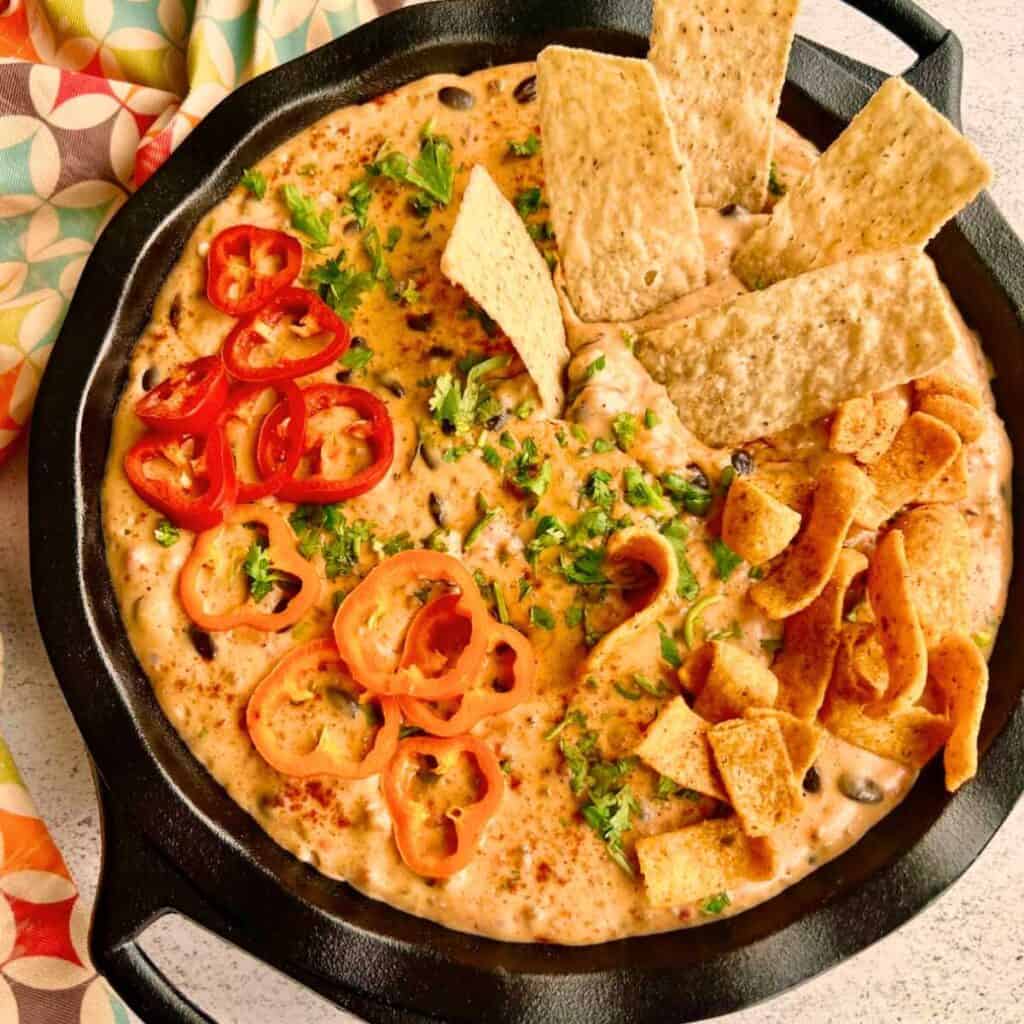 Cowboy Queso Dip in a cast iron skillet with Fritos and tortilla chips on top.