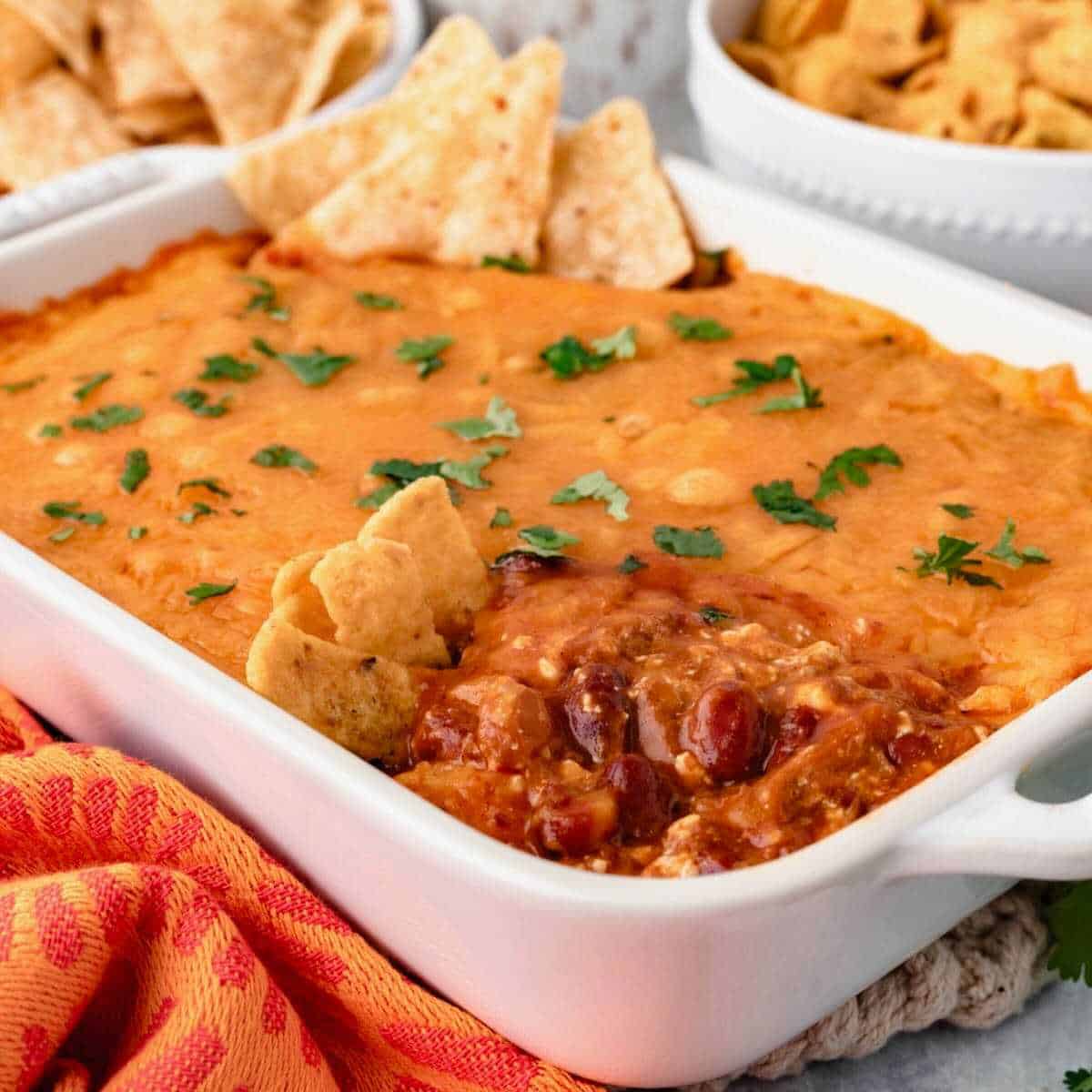 Cream cheese chili dip in a white dish with fritos and tortilla chips.