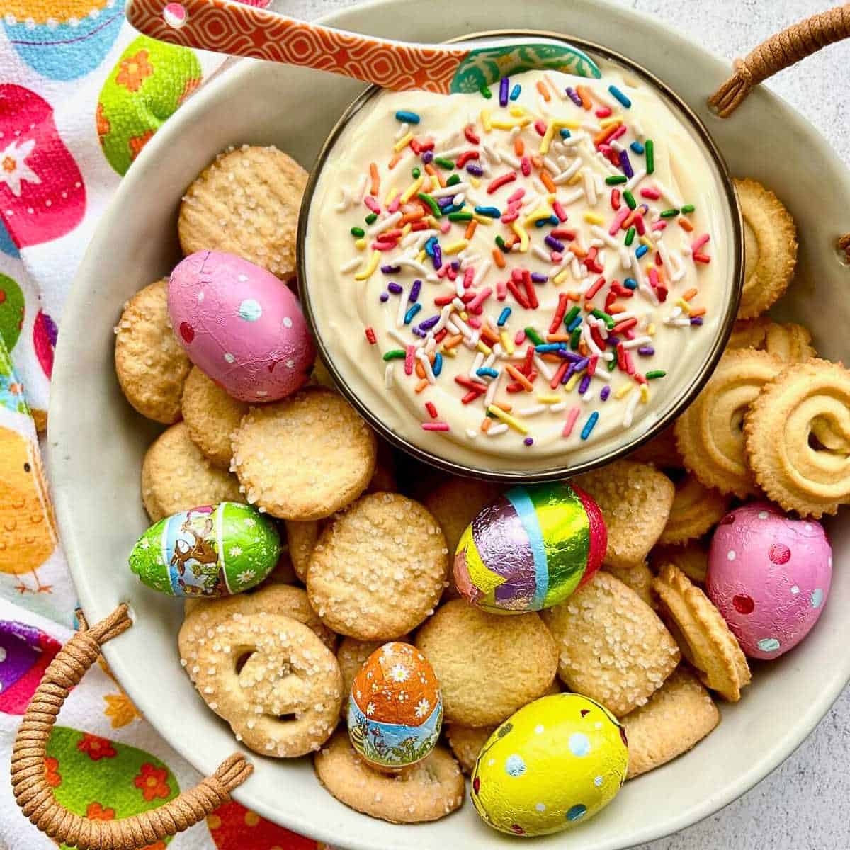 Spoon dipping into Easter Dip surrounded by chocolate eggs and butter cookies.