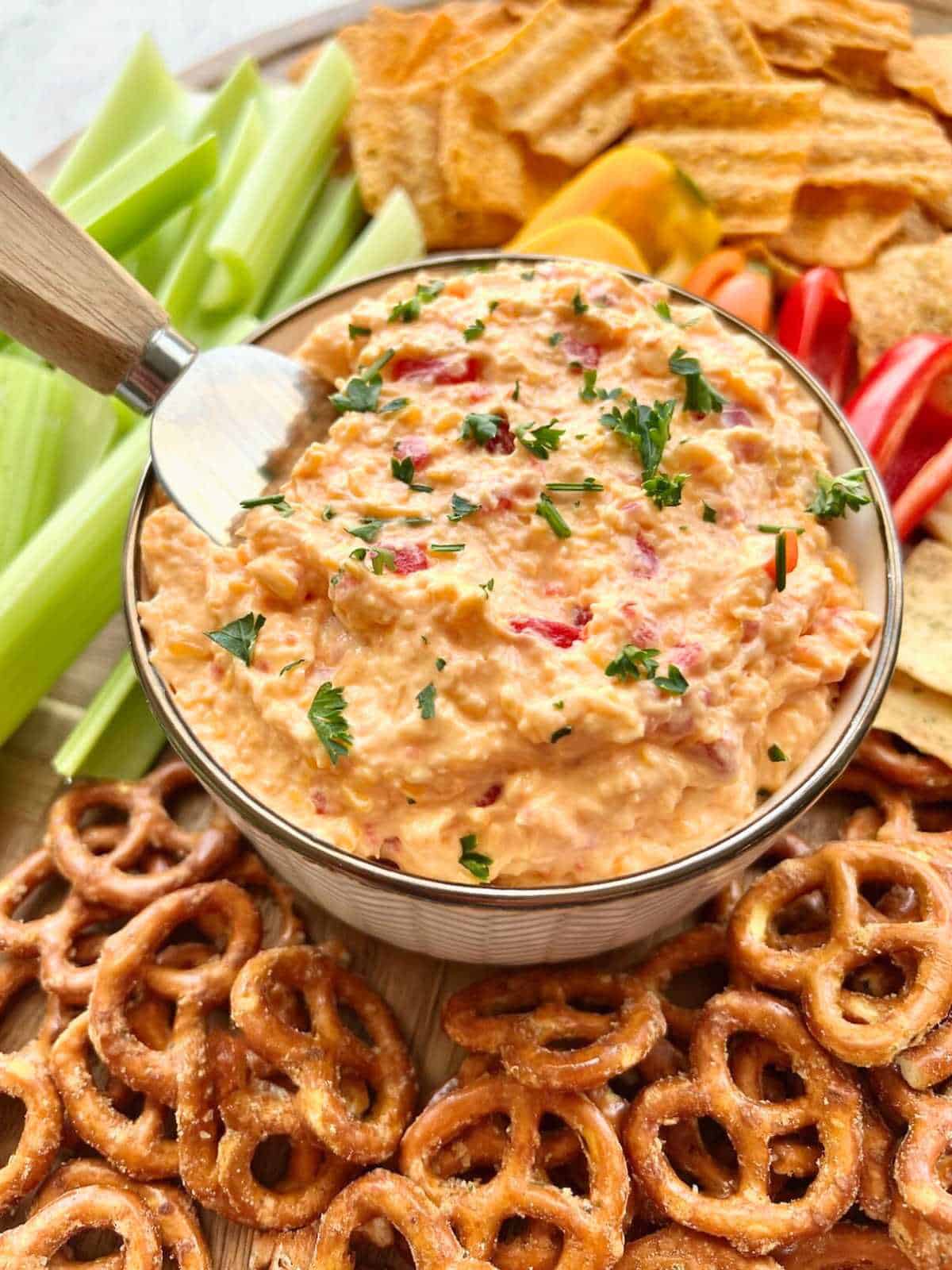 Spreader dipping out pimento cheese onto pretzels and celery.