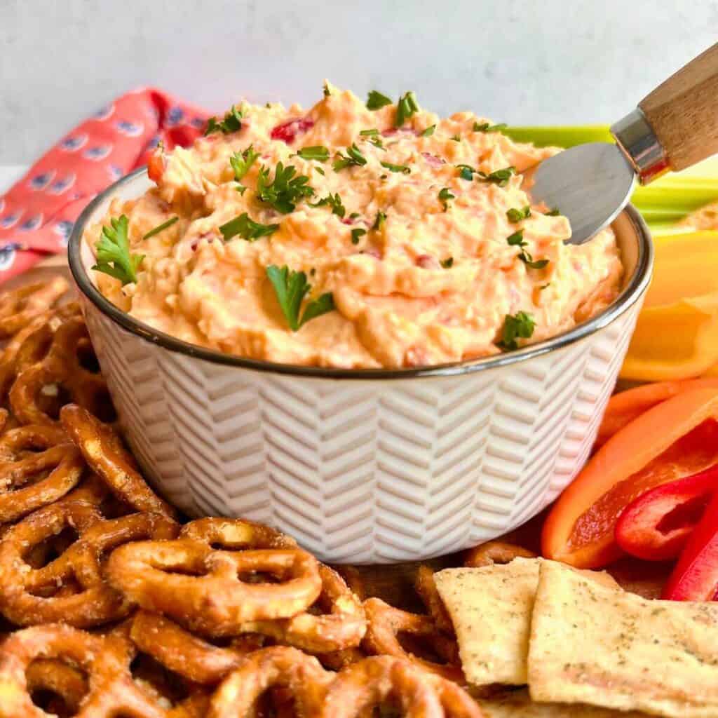 Homemade pimento cheese in a white bowl surrounded by dippers.