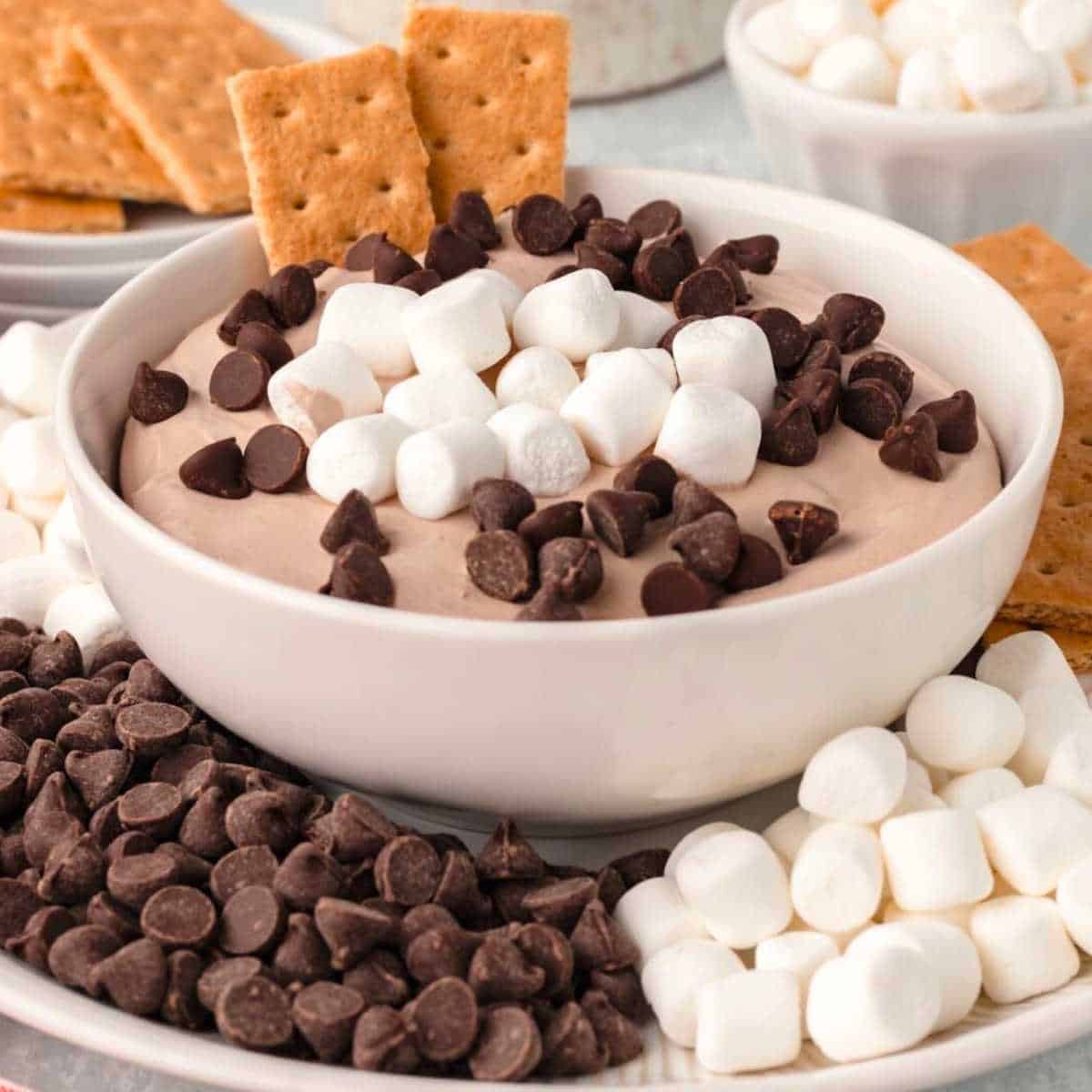 Hot cocoa dip in a white bowl topped with marshmallows and chocolate chips.