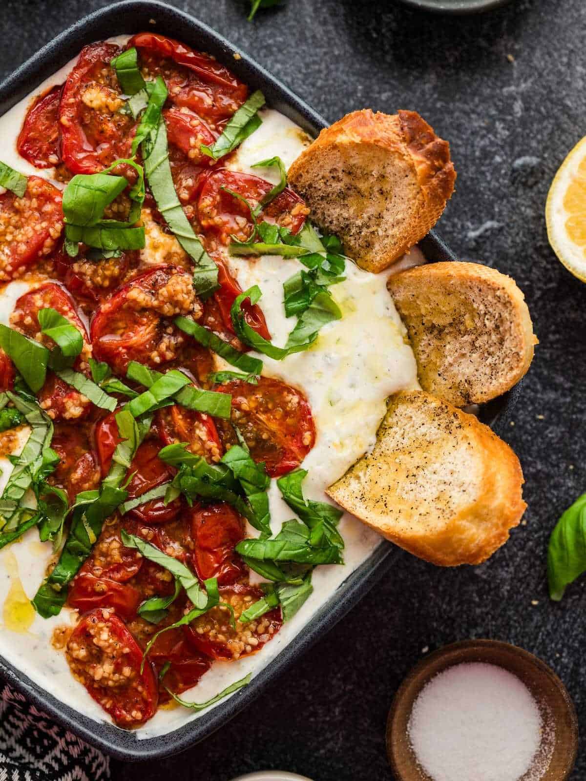 Crostini dipped into bowl of whipped feta with roasted tomatoes dip.