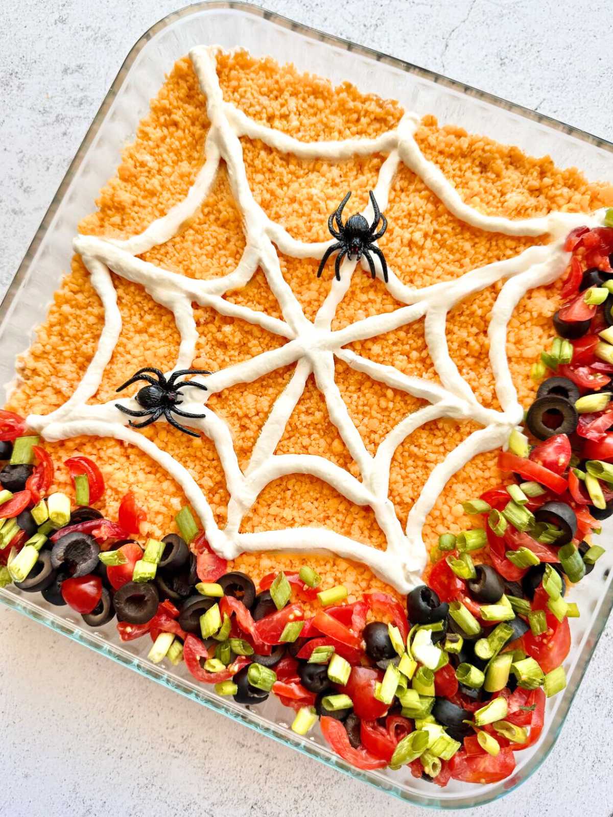 Spiders on a white sour cream spiderweb overlooking olives, green onions and tomatoes.