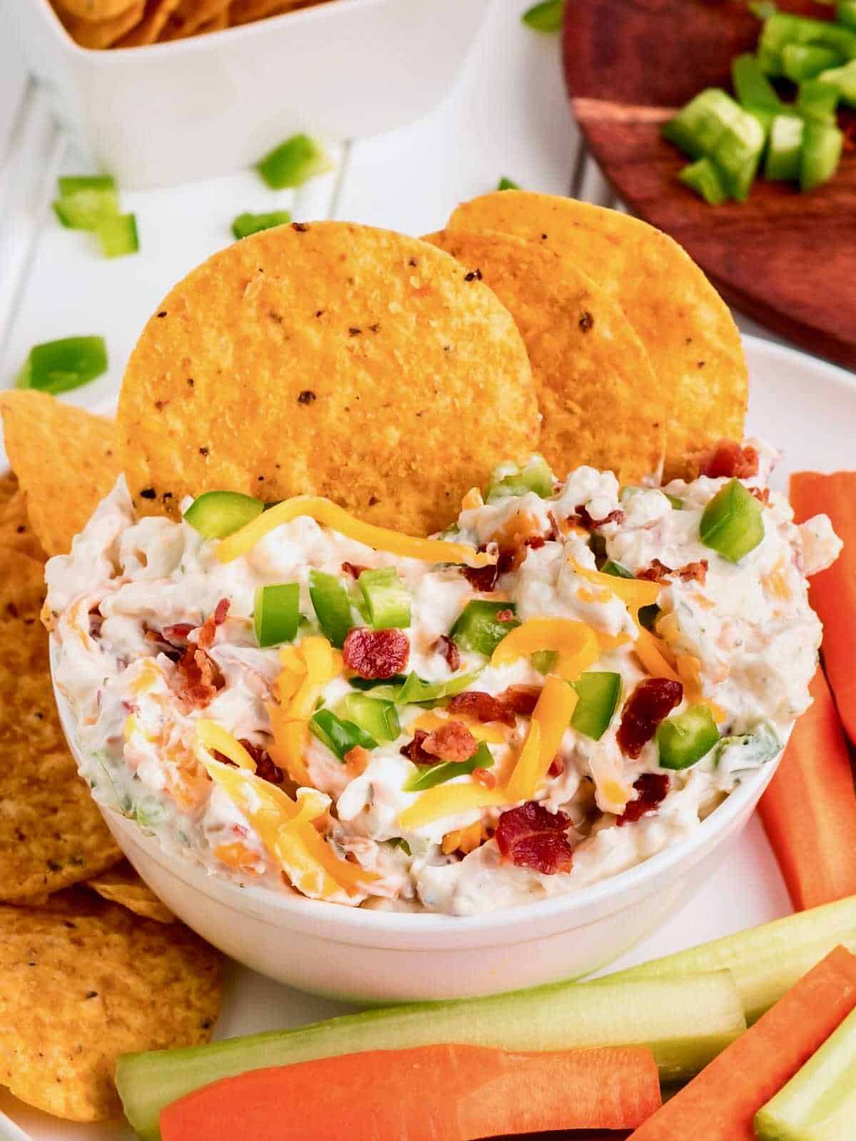 Tortilla chips dipped into a bowl of cheddar bacon dip.