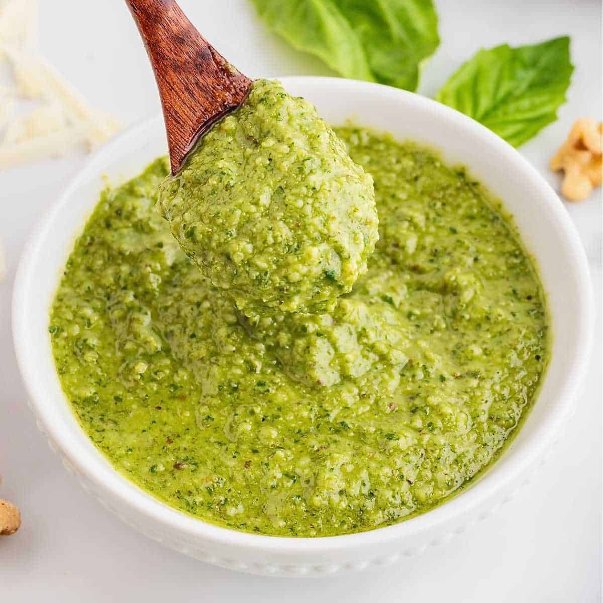 Creamy green basil pesto in a white bowl with a wooden spoon.