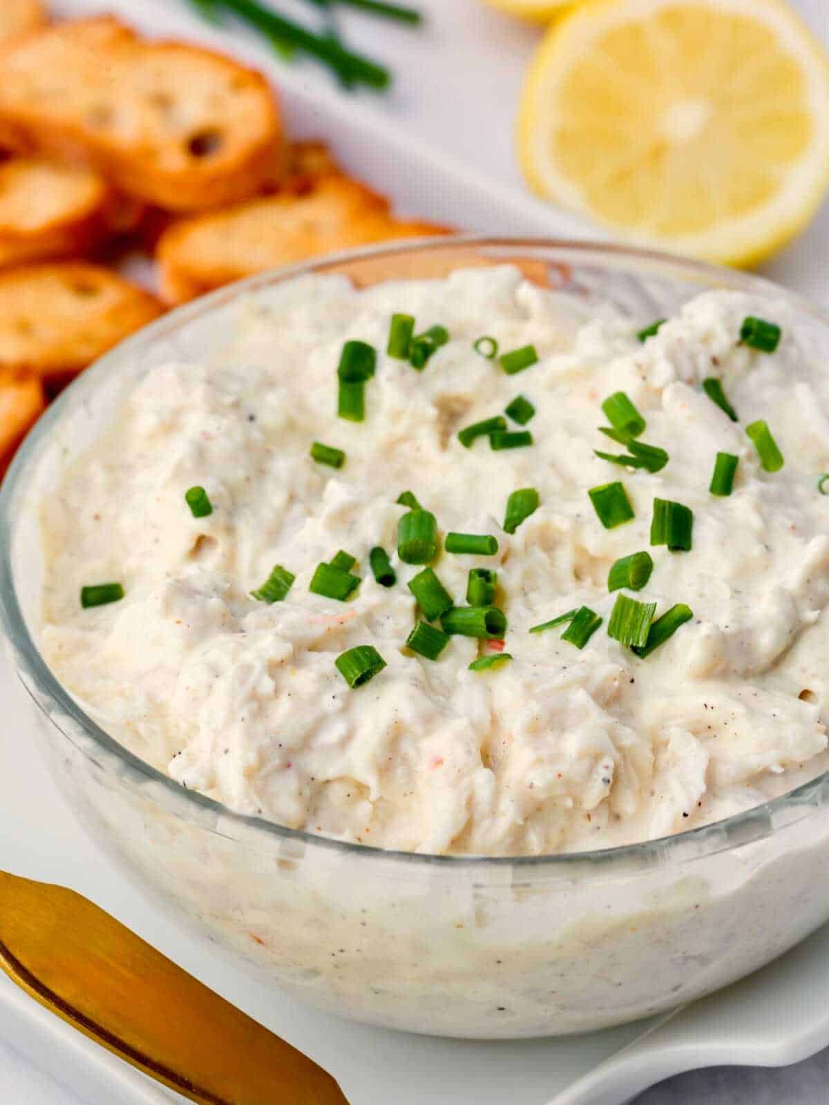Clear bowl of crab dip with chives on top.