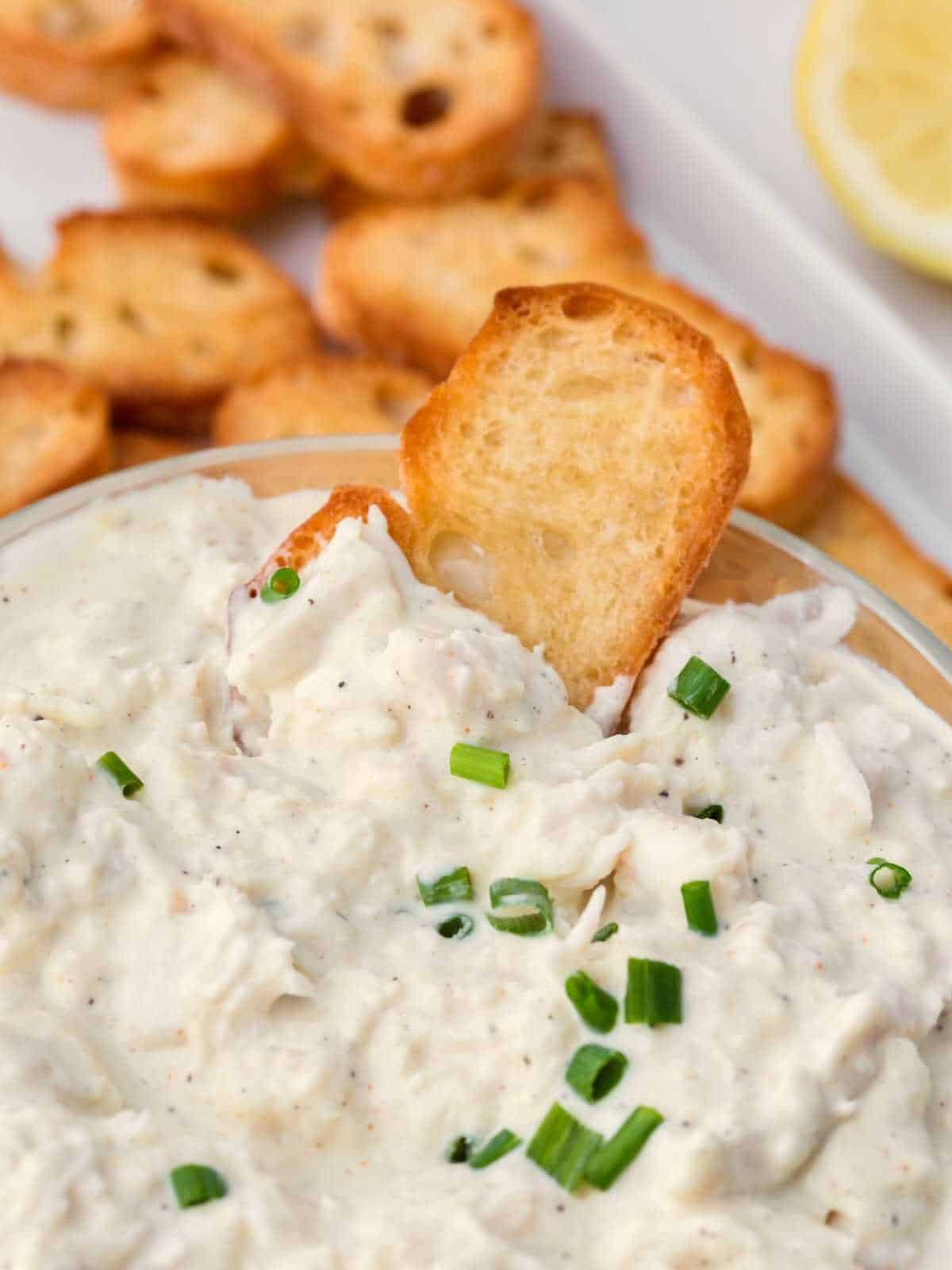 Cold crab dip in a clear dish surrounded by crostini.