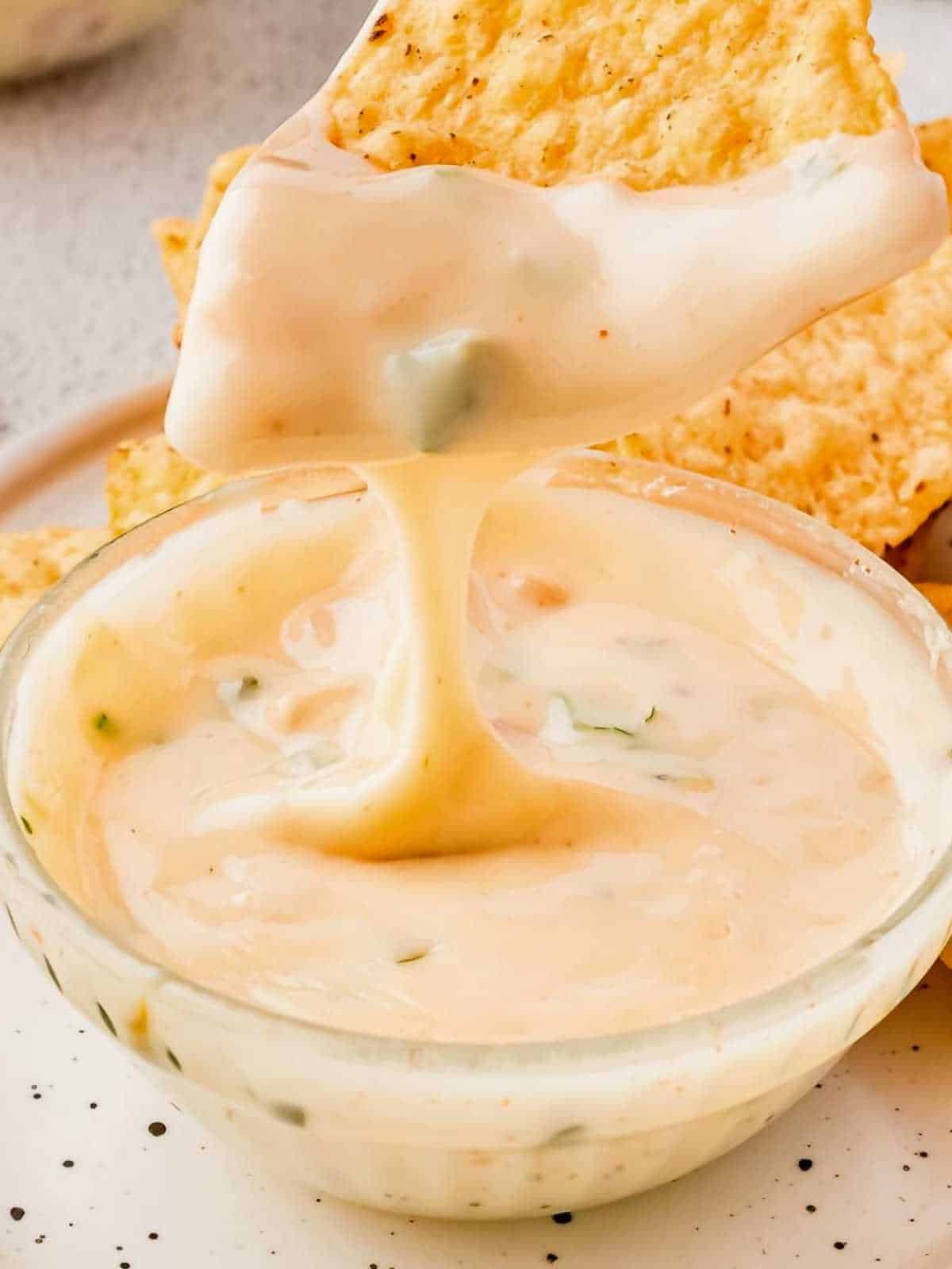 Tortilla chip being dipped in a bowl of white queso.