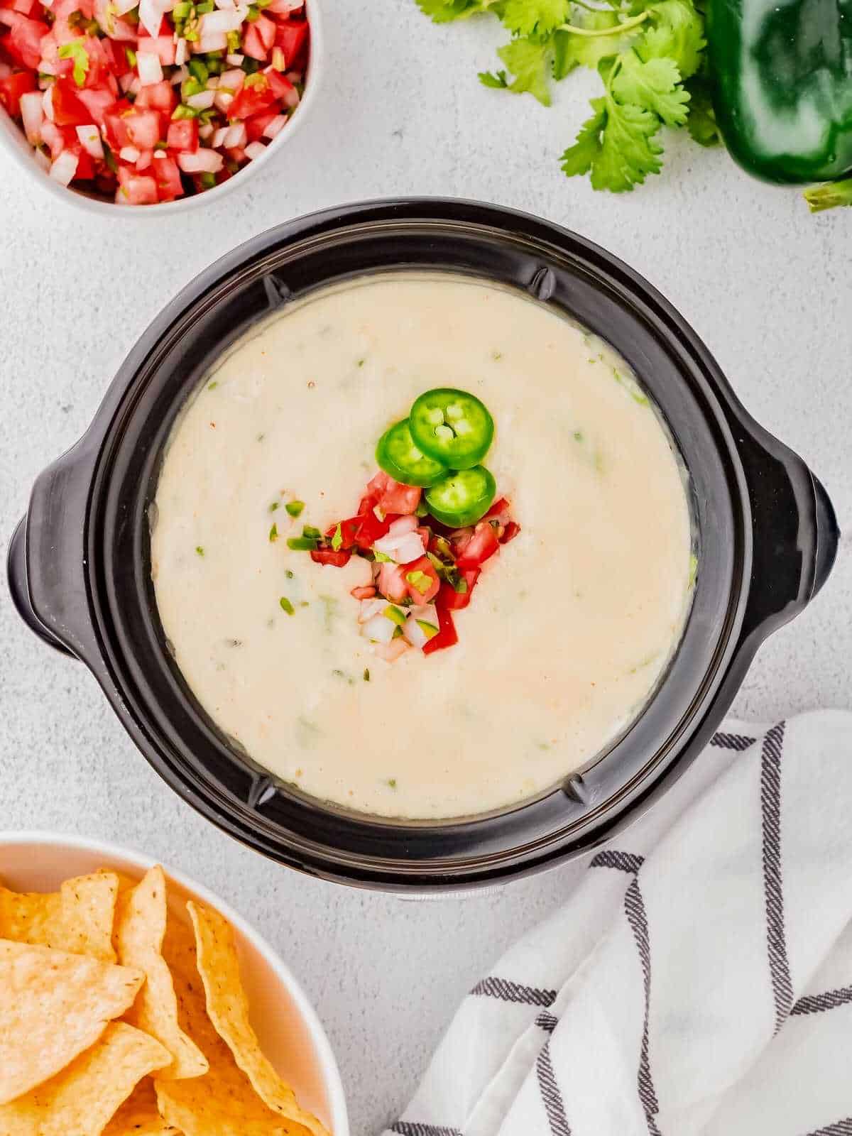 Crockpot filled with white queso and topped with pico and jalapenos.