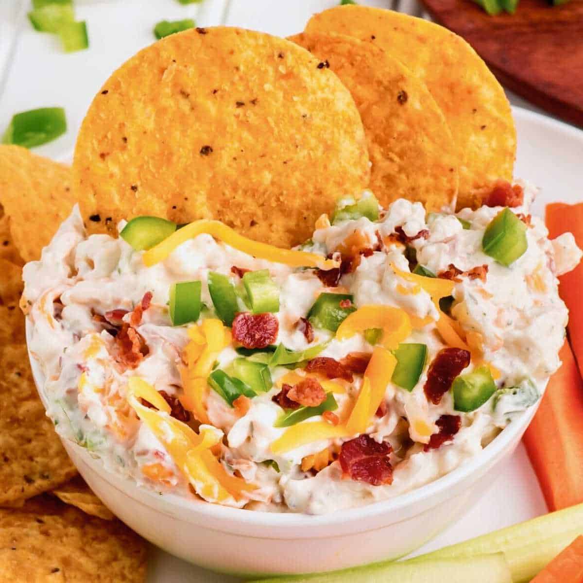 Tortilla chips dipping into a white bowl of Million Dollar Dip.