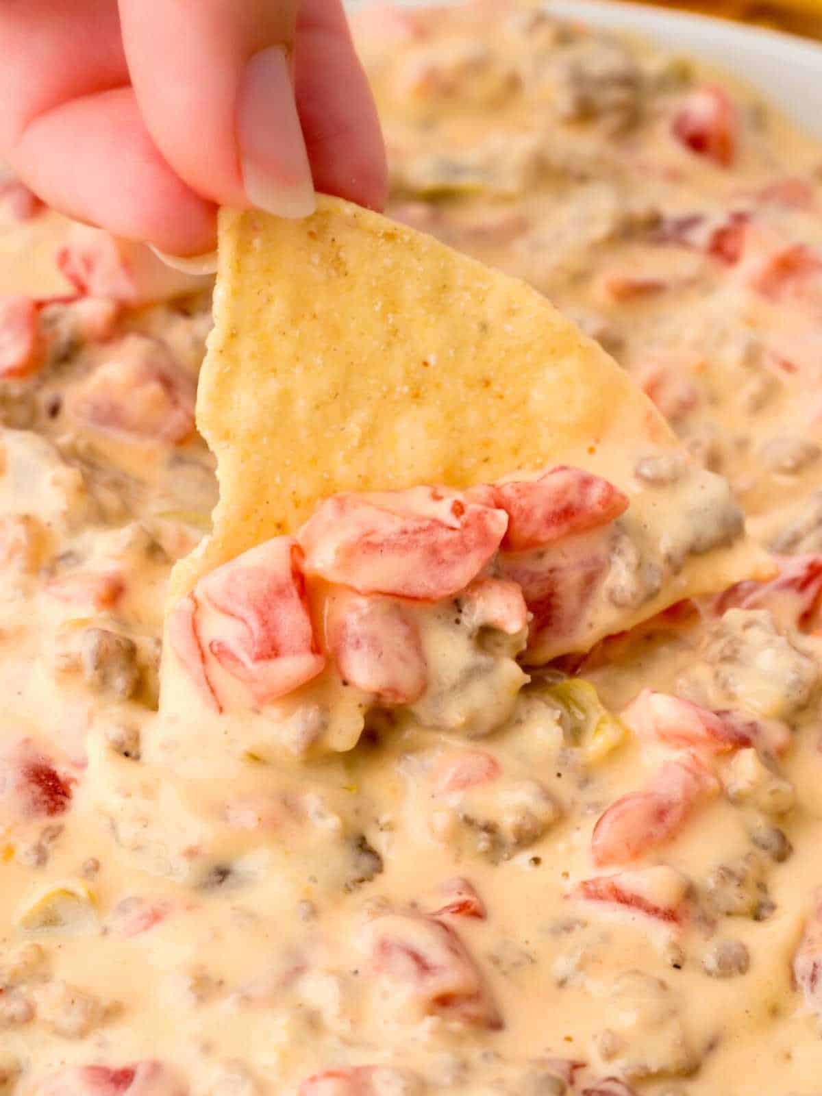 One chip being dipped into a bowl of sausage cream cheese dip with fingers.