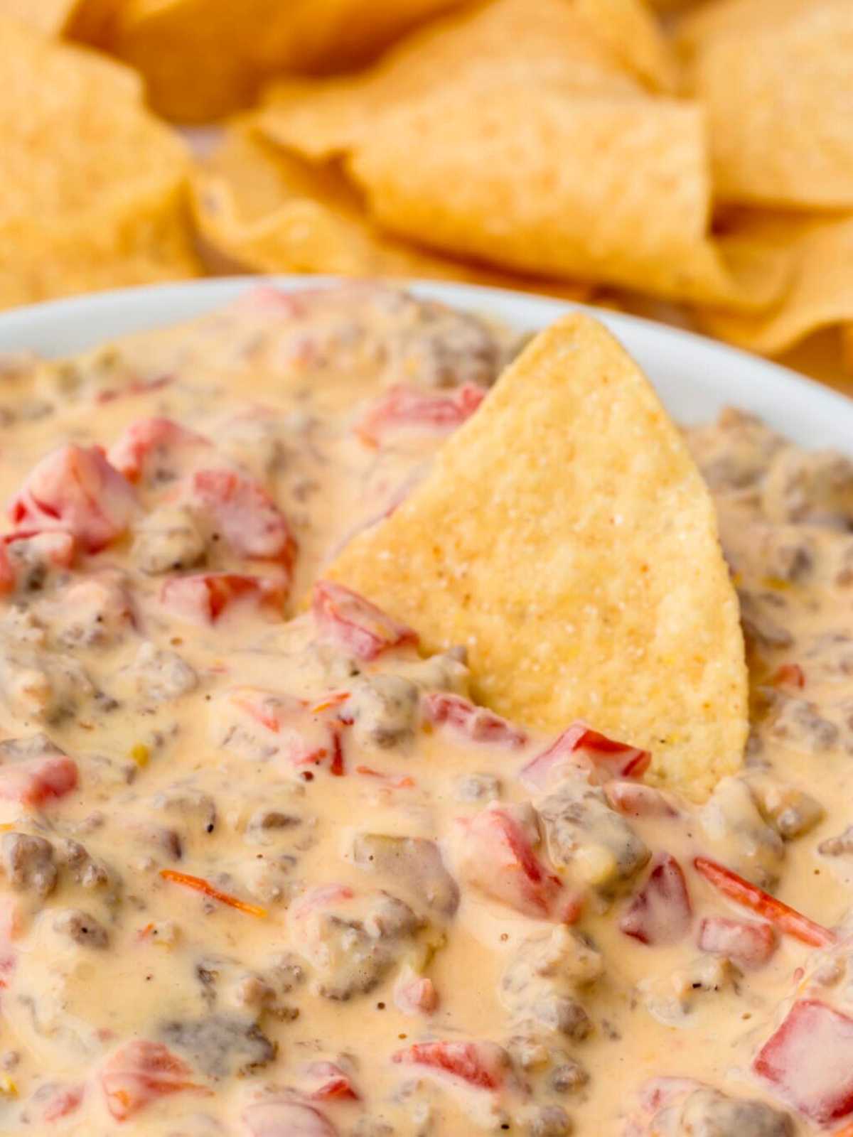 Tortilla Chip dipping into a bowl of Rotel Sausage Dip with cream cheese and Velveeta.