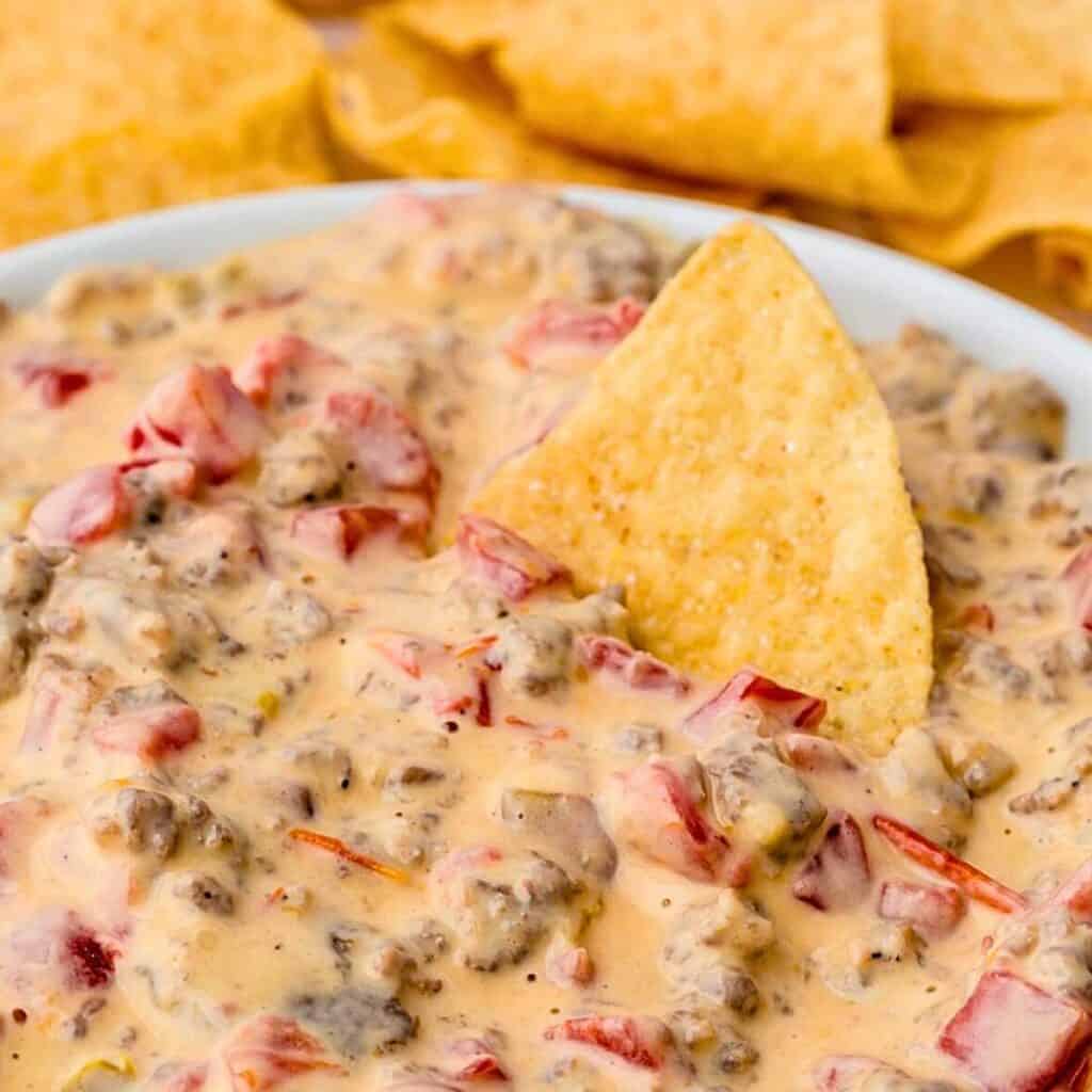 Tortilla chip dipped into a bowl of cream cheese sausage dip.