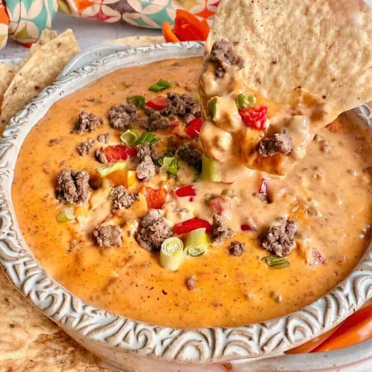 Slow Cooker Rotel Dip dripping off a tortilla chip into a bowl with ground beef and toppings.