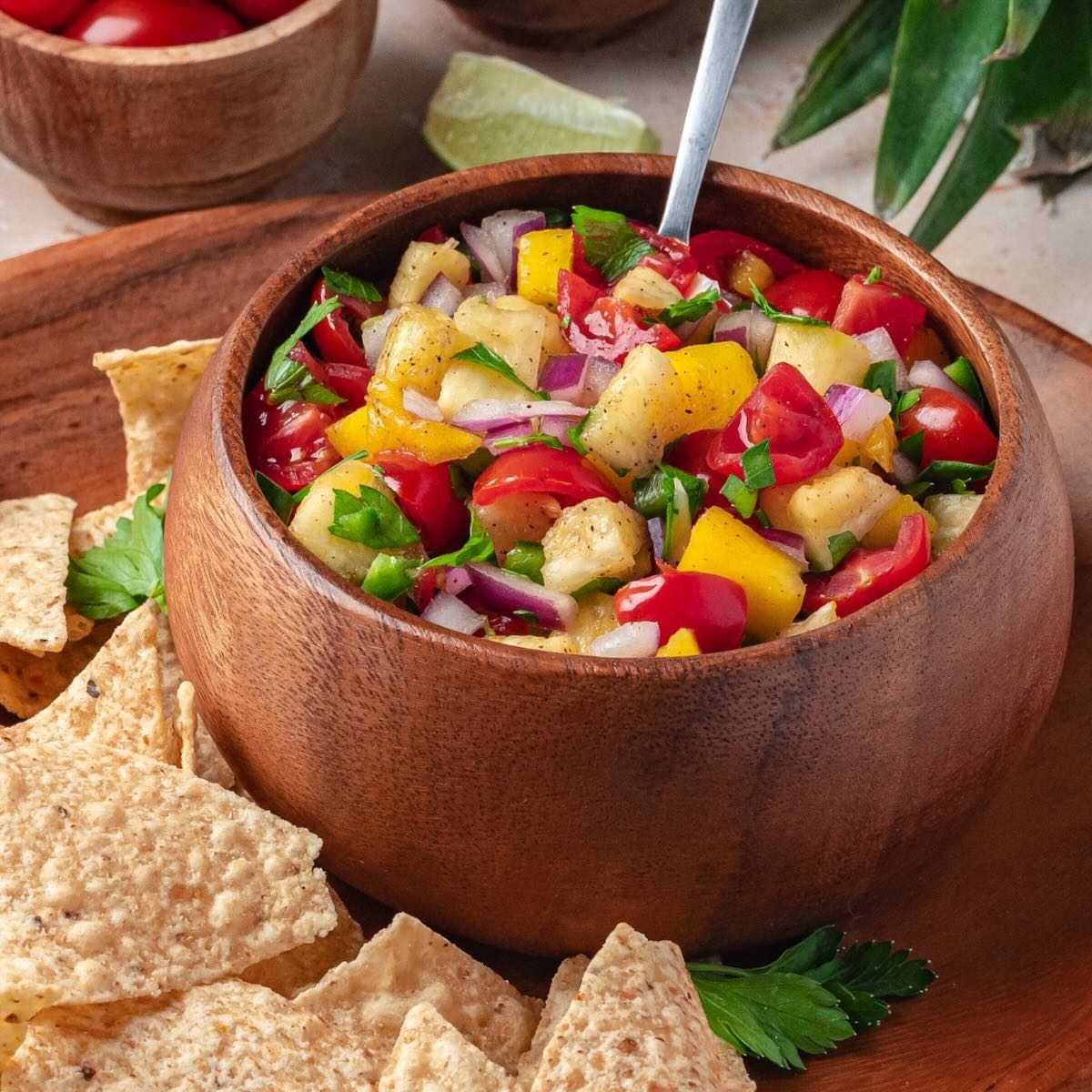 Mango pineapple salsa with cilantro and tomatoes in a wooden bowl.
