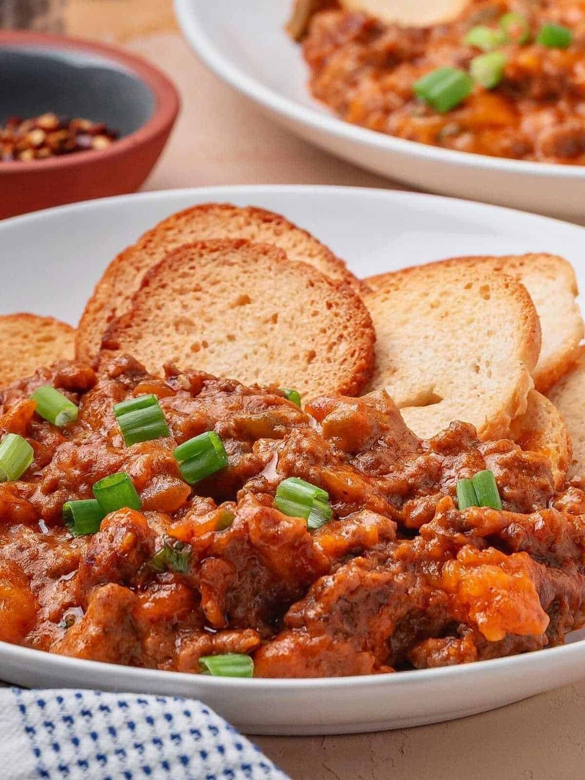 Sloppy Joe Dip with bagel chips on a while plate and blue checkered cloth.
