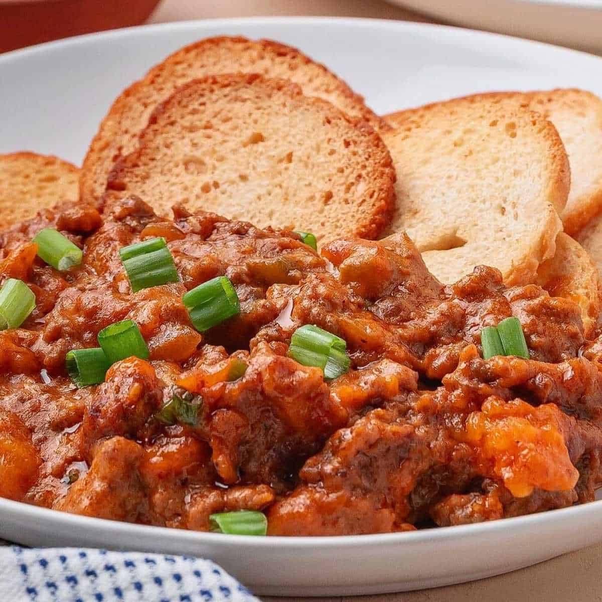 Sloppy Joe Dip with green onions and bagel chips on a white plate.
