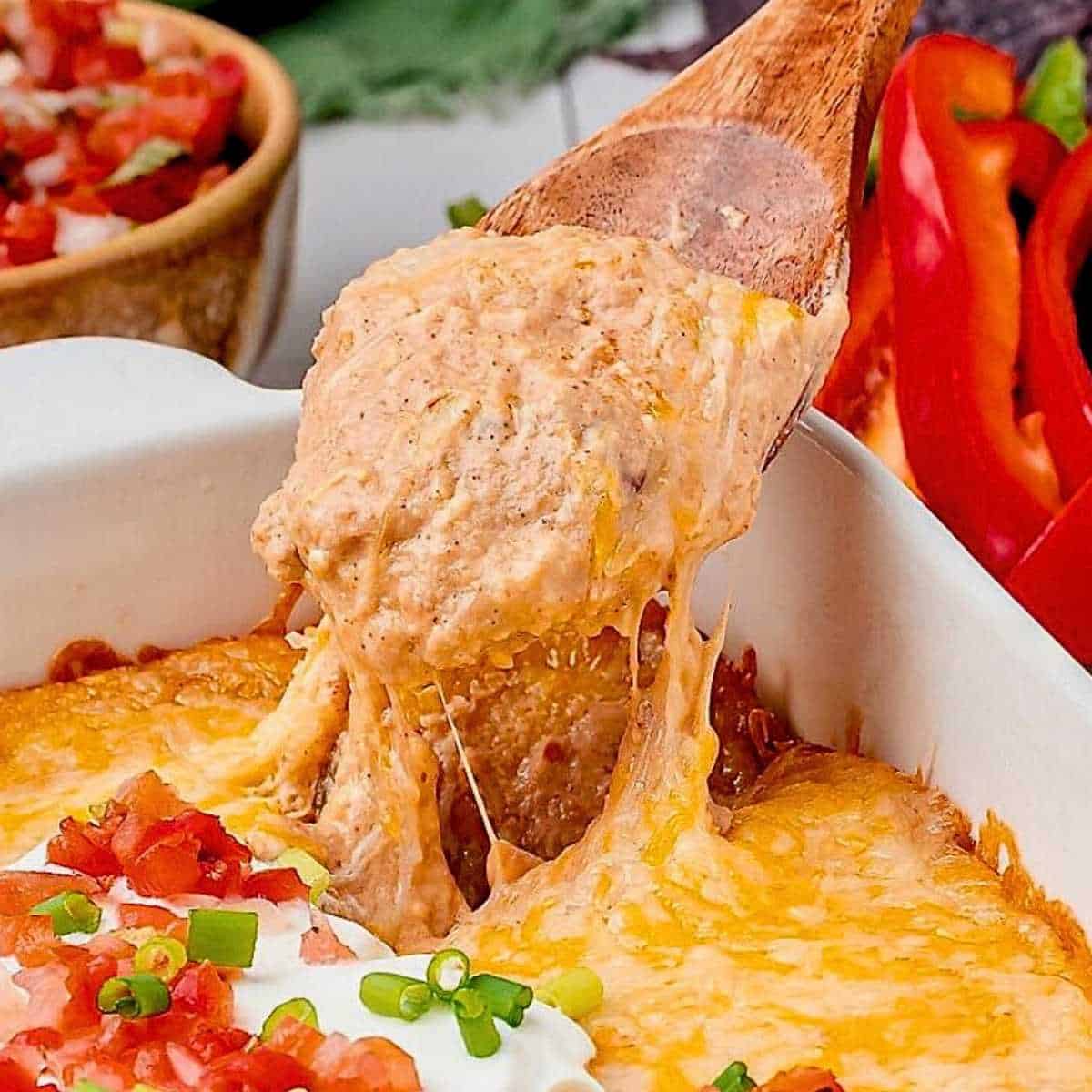 Wooden spoon dipping into a casserole dish of Texas Trash dip with sour cream.