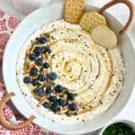 Whipped Feta with Honey in a white round dish with blueberries, almonds and crushed red pepper flakes on top.