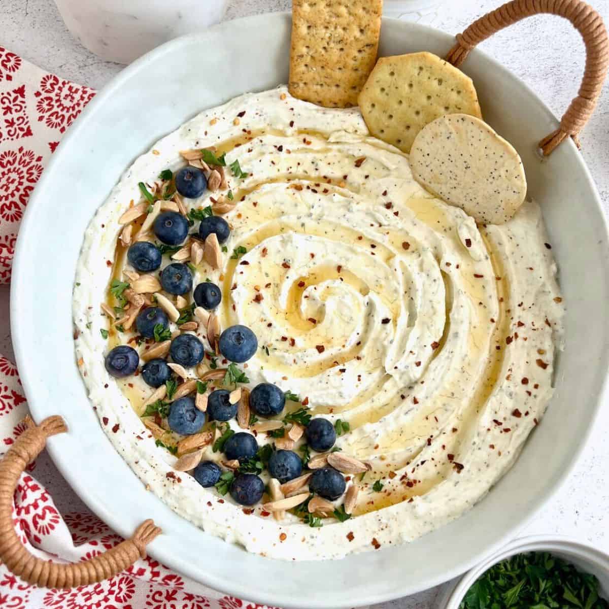 Whipped Feta with Honey in a white round dish with blueberries, almonds and crushed red pepper flakes on top.