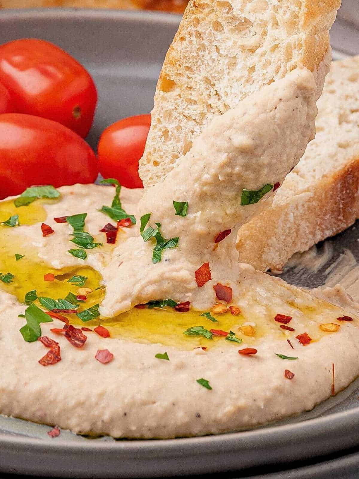 Bread dipping into white bean dip spread on a plate.