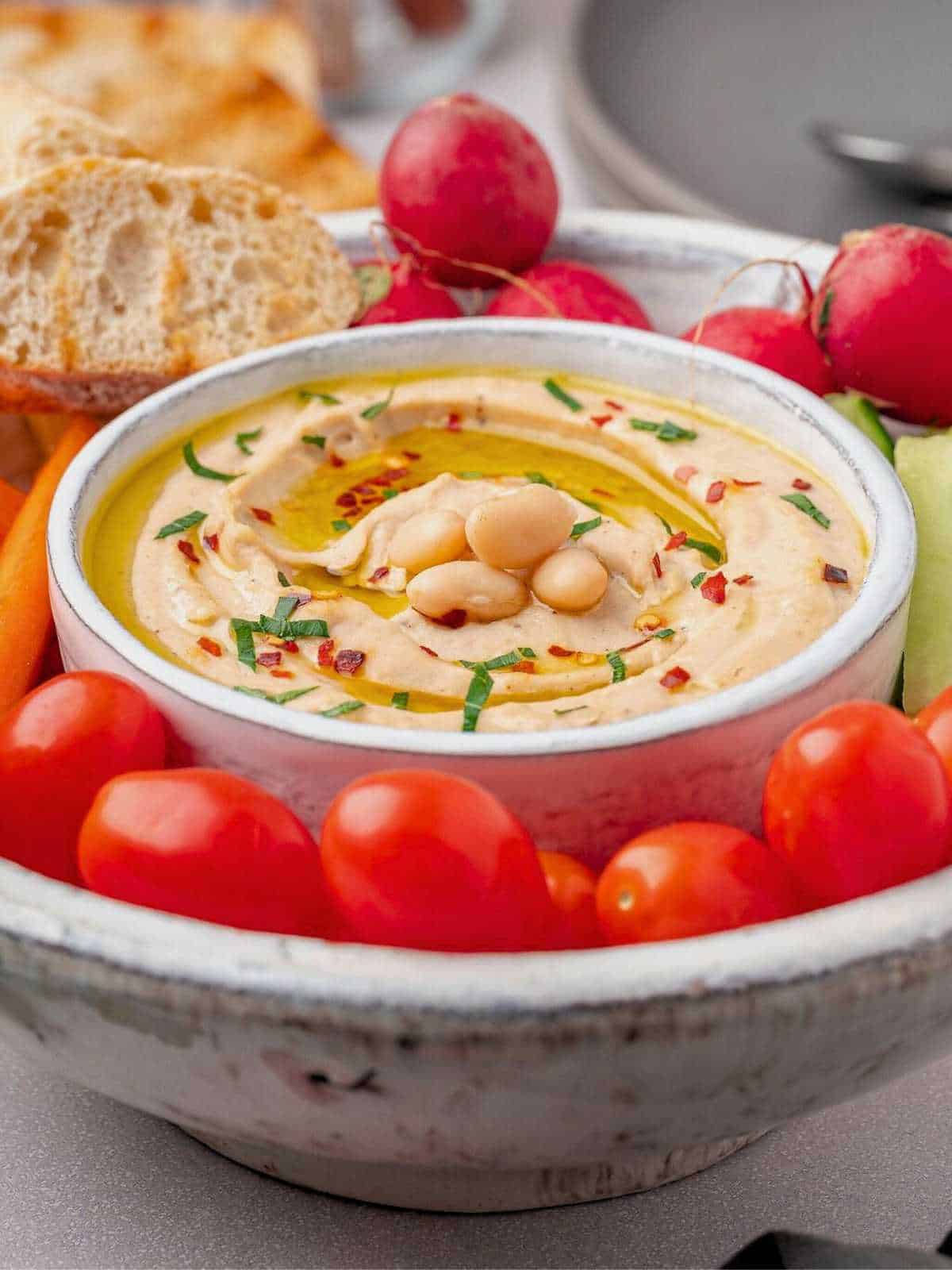 Cannellini bean dip in a white bowl with veggies.