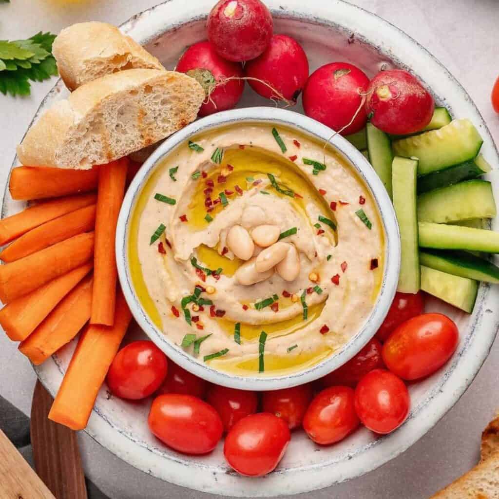 White bean dip surrounded by radishes, carrots, tomatoes and cucumbers.