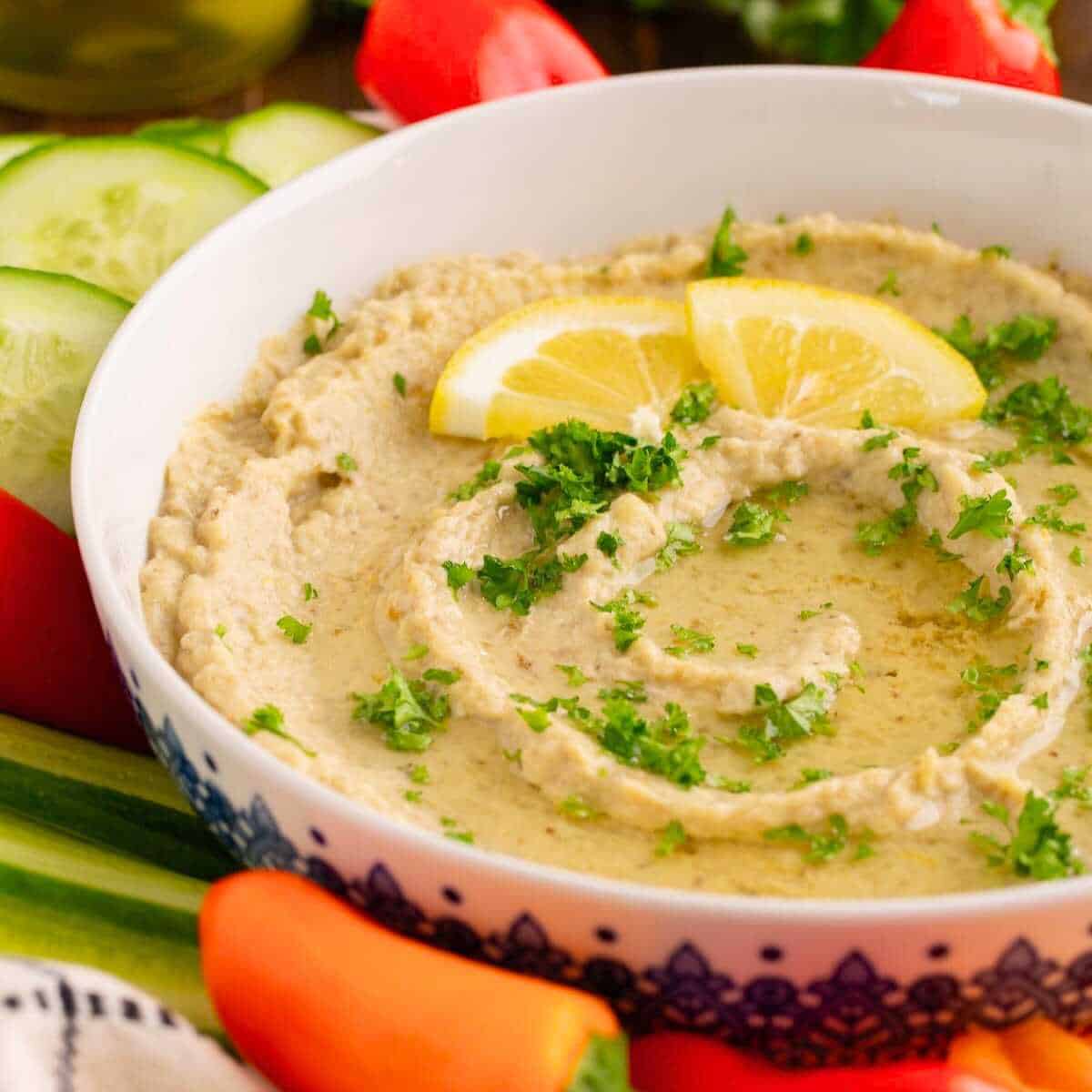 Baba ganoush, a roasted eggplant dip, in a white bowl surrounded by colorful peppers.