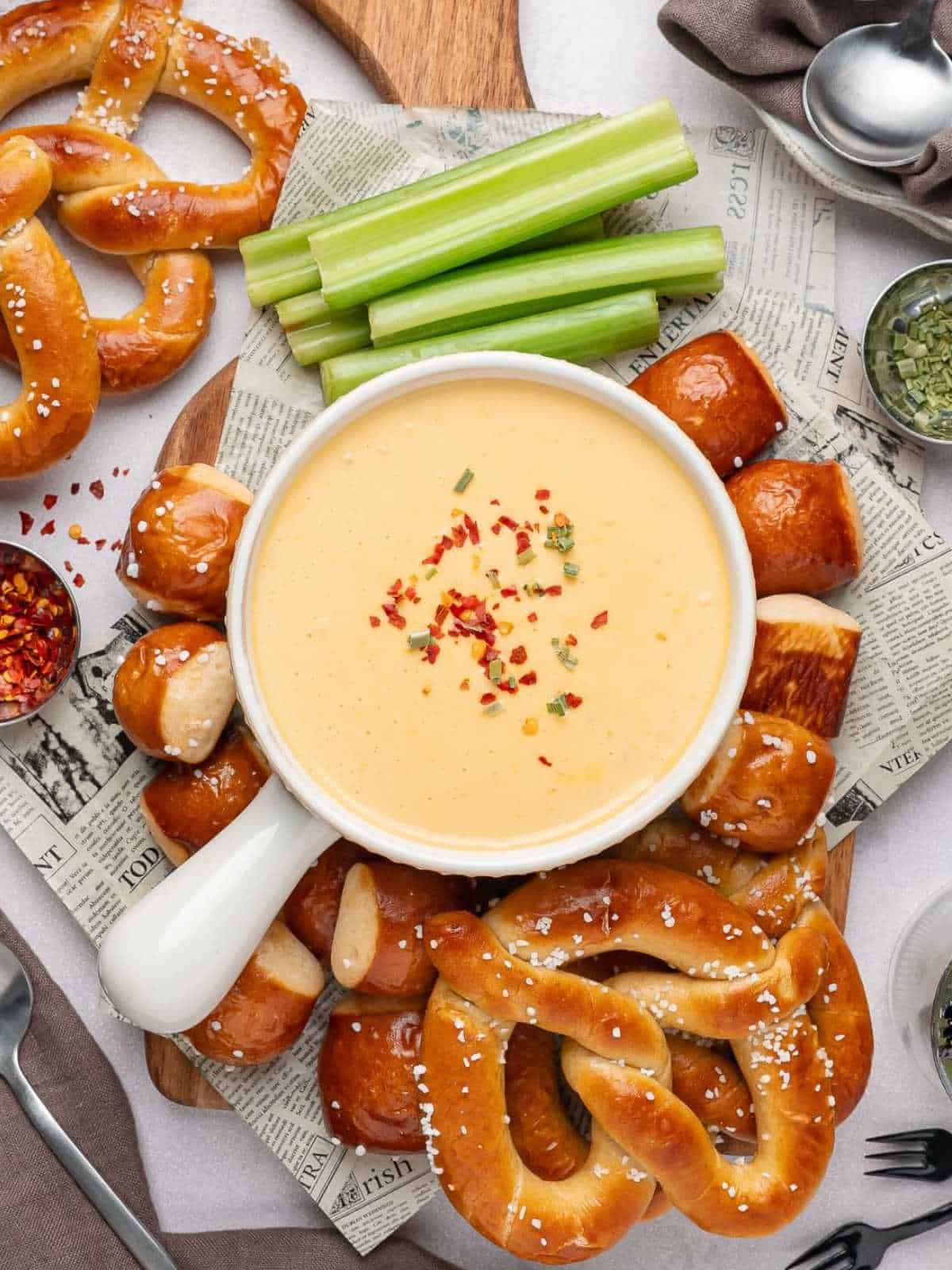 Beer cheese pretzel dip in a white bowl on newspapers with pretzels and celery.