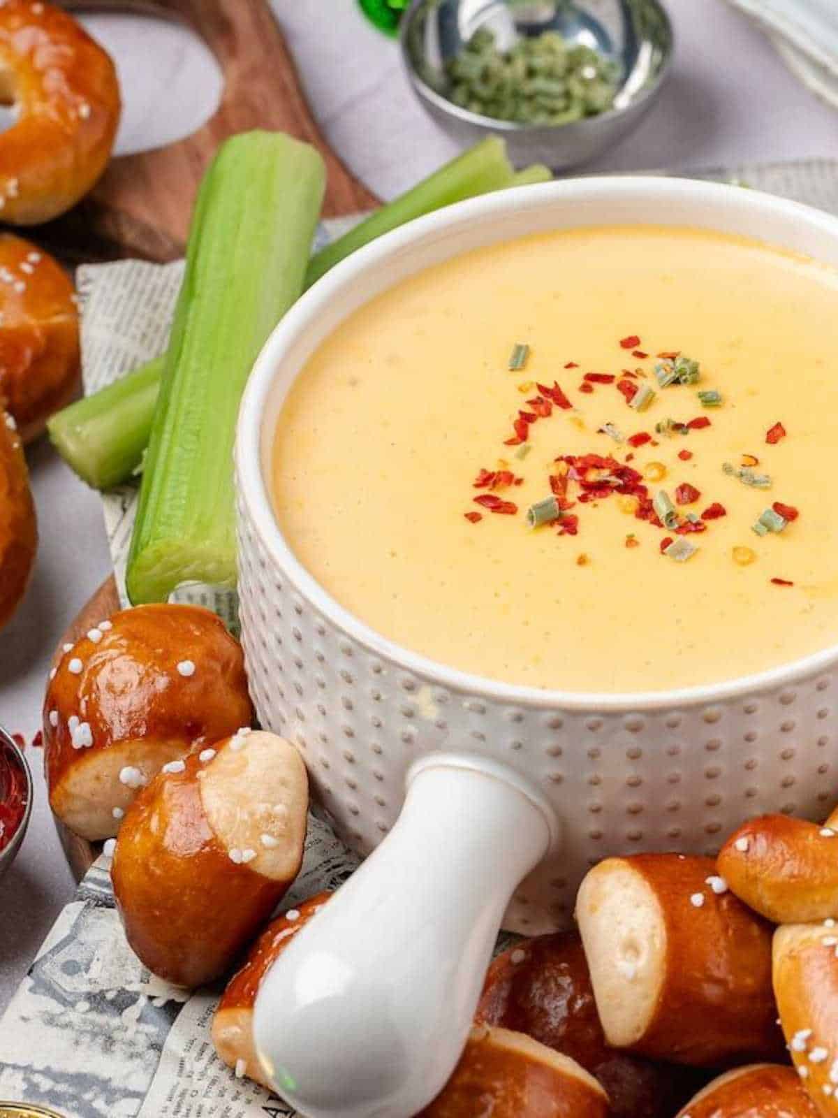 White bowl of beer cheese dip surrounded by pretzels and celery.