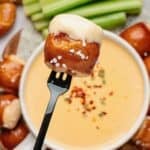 Beer cheese pretzel dip being lifted out of a bowl by a pretzel bite on a fork.