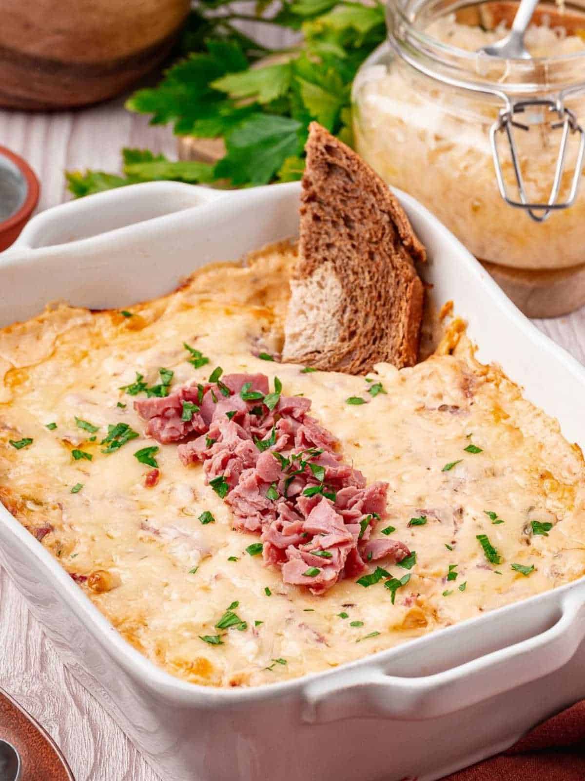 Reuben dip in a white dish with rye bread dipping into it.