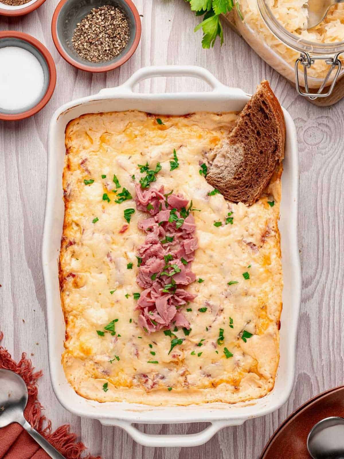 Baking dish filled with reuben dip garnished with corned beef.