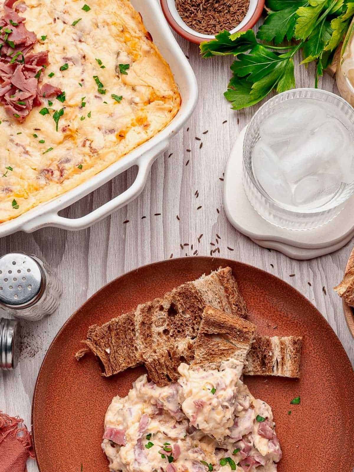 Rust colored plate with reuben dip and rye bread surrounded by other ingredients.