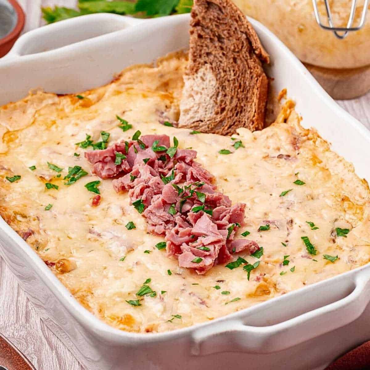 Reuben Dip in a white baking dish with cheese and corned beef on top.