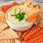 Avocado Ranch Dip with limes on top surrounded by chips and carrots.