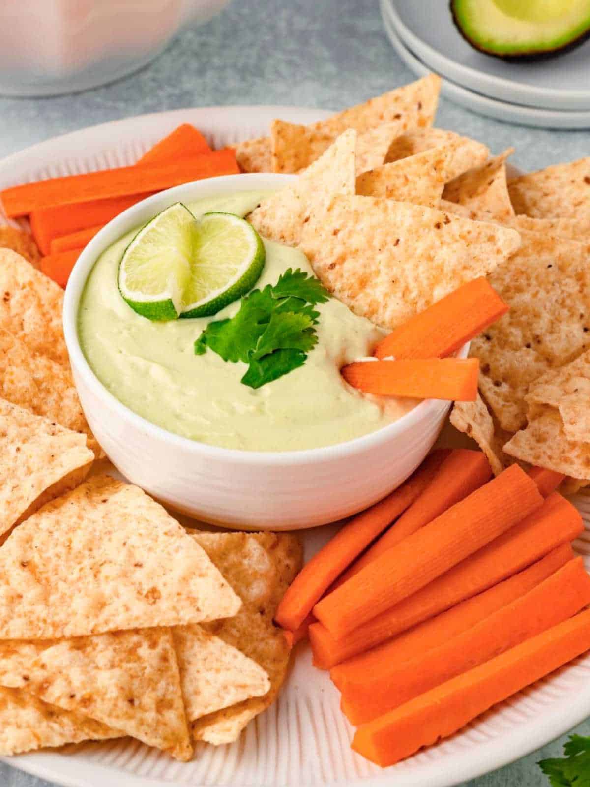 Avocado Ranch Dip with carrots and tortilla chips on a white plate.