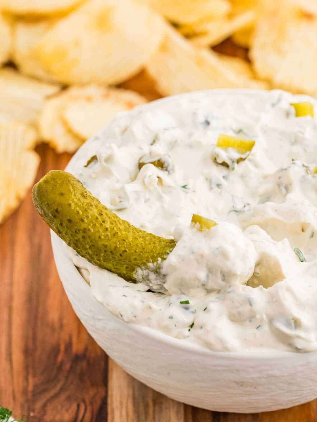 Dill pickle dipping into a bowl of pickle dip.