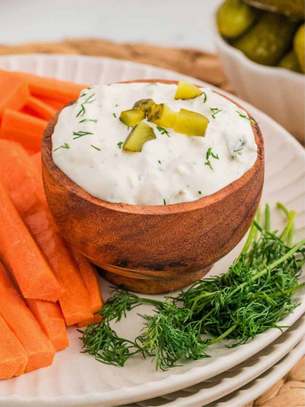 Pickles garnishing a wooden bowl of dill pickle dip with carrots on the side.