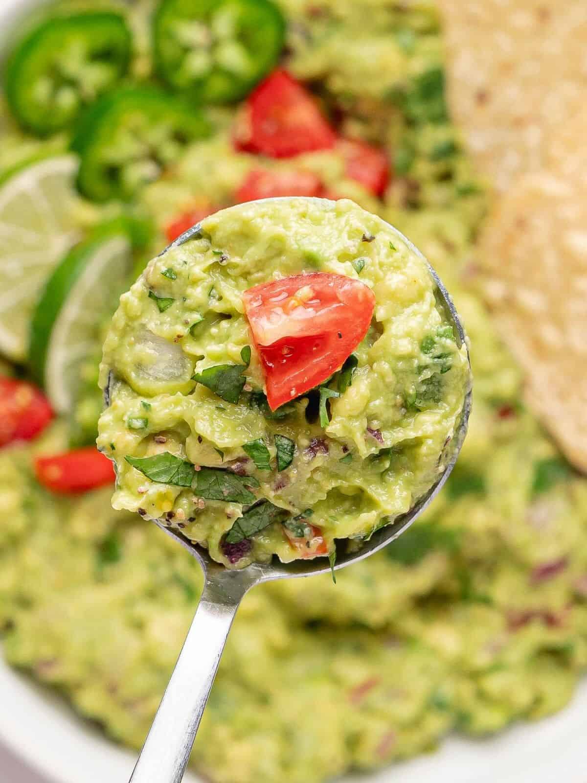 A big scoop of guacamole lifted up by a spoon.