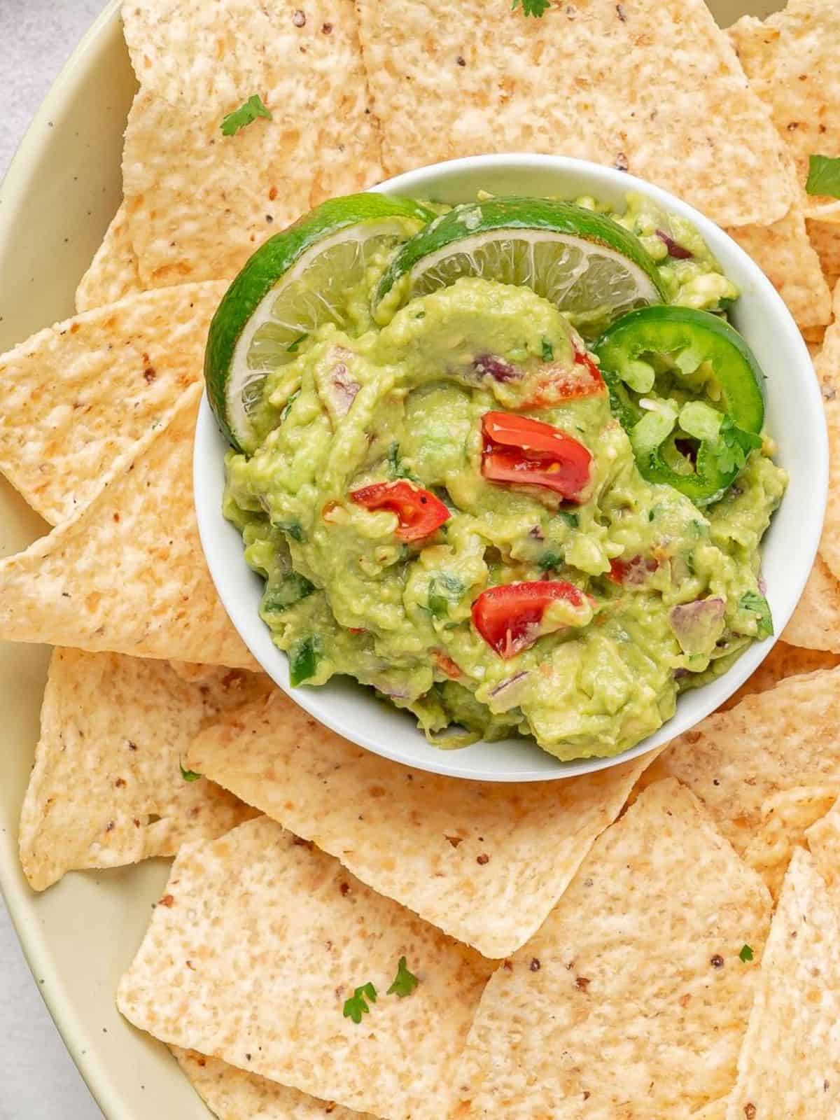 White bowl of guacamole surrounded by tortilla chips.