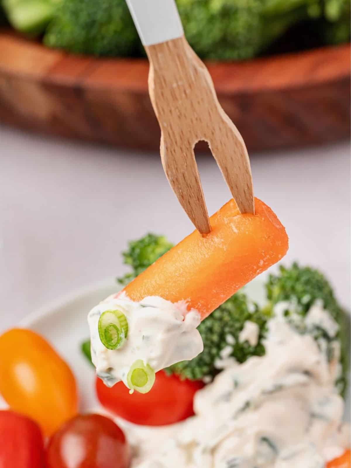Carrot on a fork dipping into spinach dip.