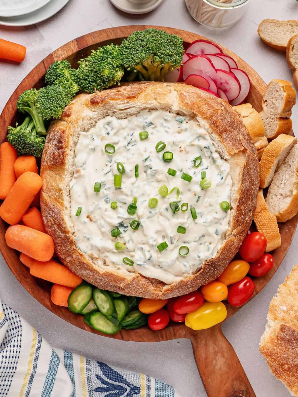 Bread bowl filled with Knorr Spinach Dip surrounded by carrots, broccoli, radishes, tomatoes and cucumbers.